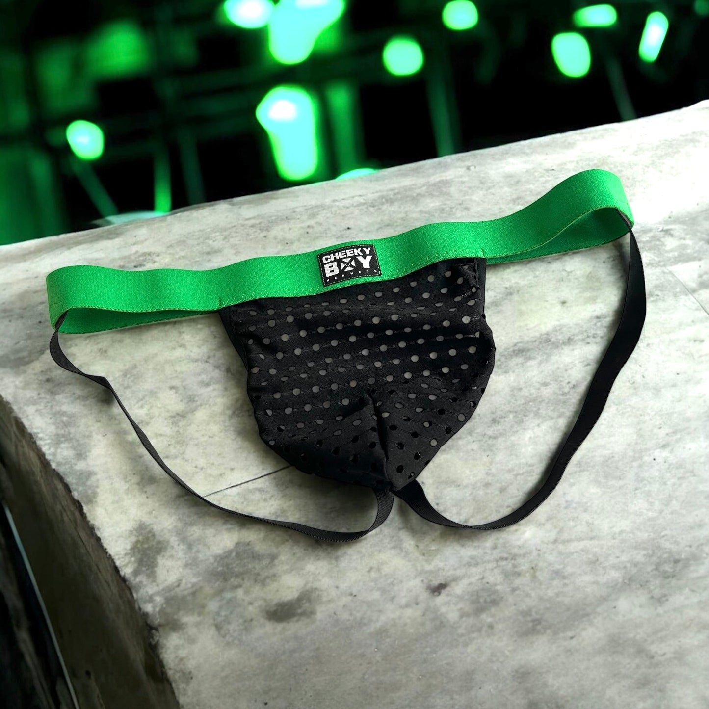 Men’s black mesh jockstrap with green elastic waistband, featuring a Cheeky Boy Harness black and white logo at the centre front, and black rear straps.