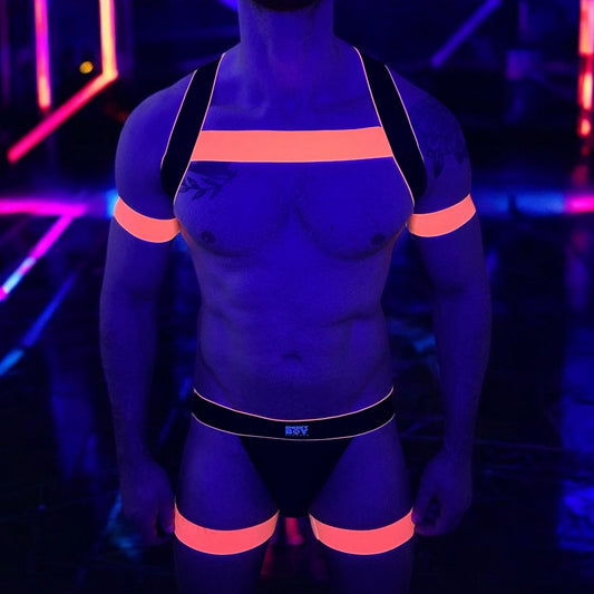 Man wearing a handmade black and neon orange elastic body harness with matching bicep bands, jockstrap, and thigh bands by Cheeky Boy Harness in a nightclub setting