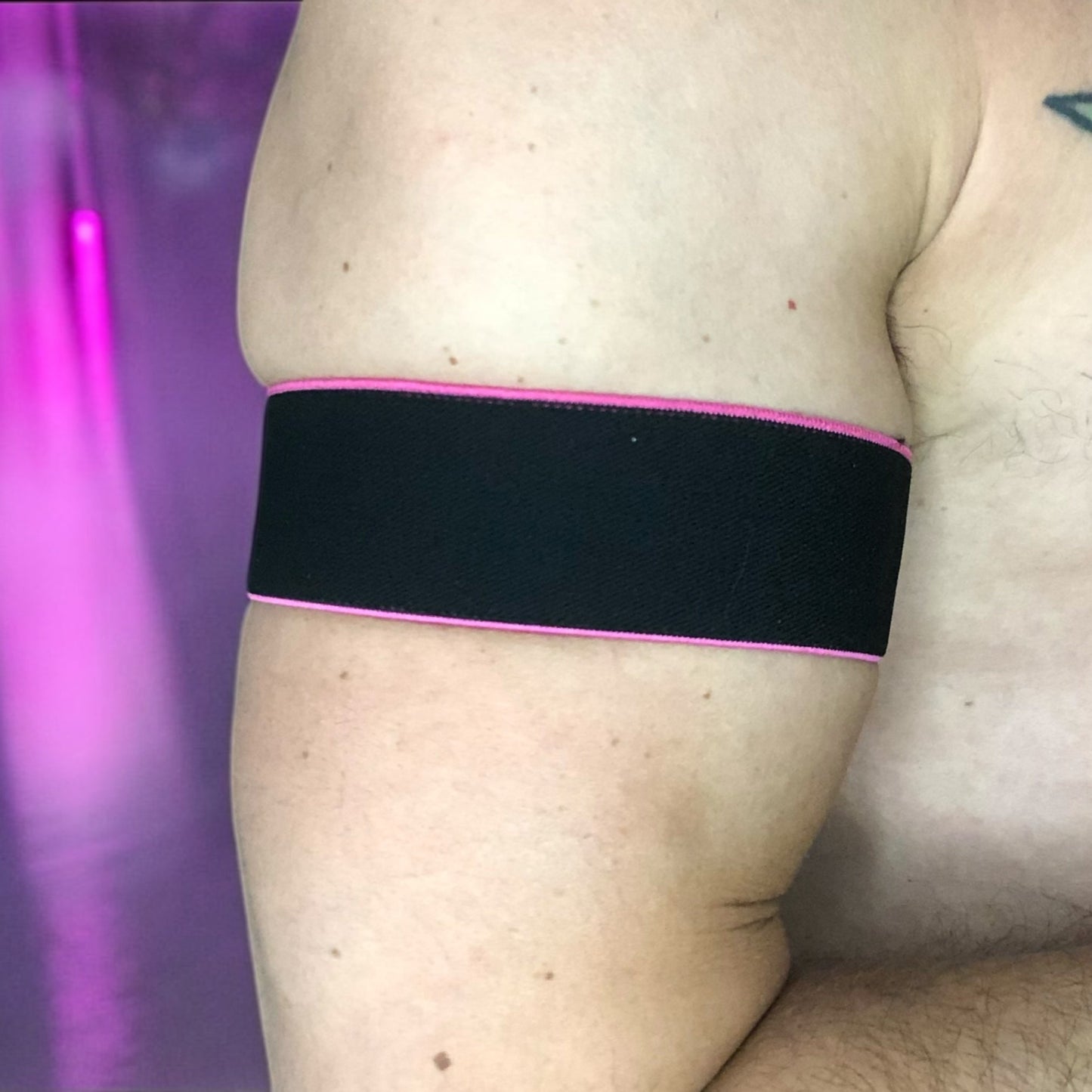 Man wearing a handmade black chest harness with glowing neon orange edges, styled in a Spartan warrior design. Includes matching bicep bands. Photographed in a neon-lit club setting. The harness is made to measure and glows under UV light, ideal for clubbing and festival wear.