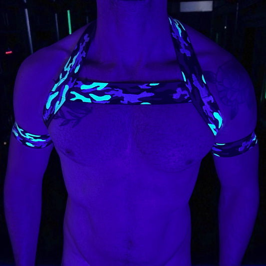 Toned Man wearing a custom-fit green and black camo print elastic chest harness and matching jockstrap set with bicep and thigh bands, by Cheeky Boy Harness. Festival and clubwear set photographed against a neon green camo staircase backdrop.