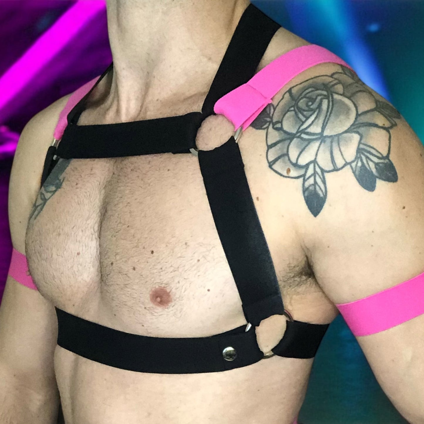 Model wearing a Cheeky Boy Harness custom-fit mens black and hot pink elastic chest and body harness, paired with matching bicep bands, leg straps, and a black mesh jockstrap. The outfit is styled for clubwear or fetish events.