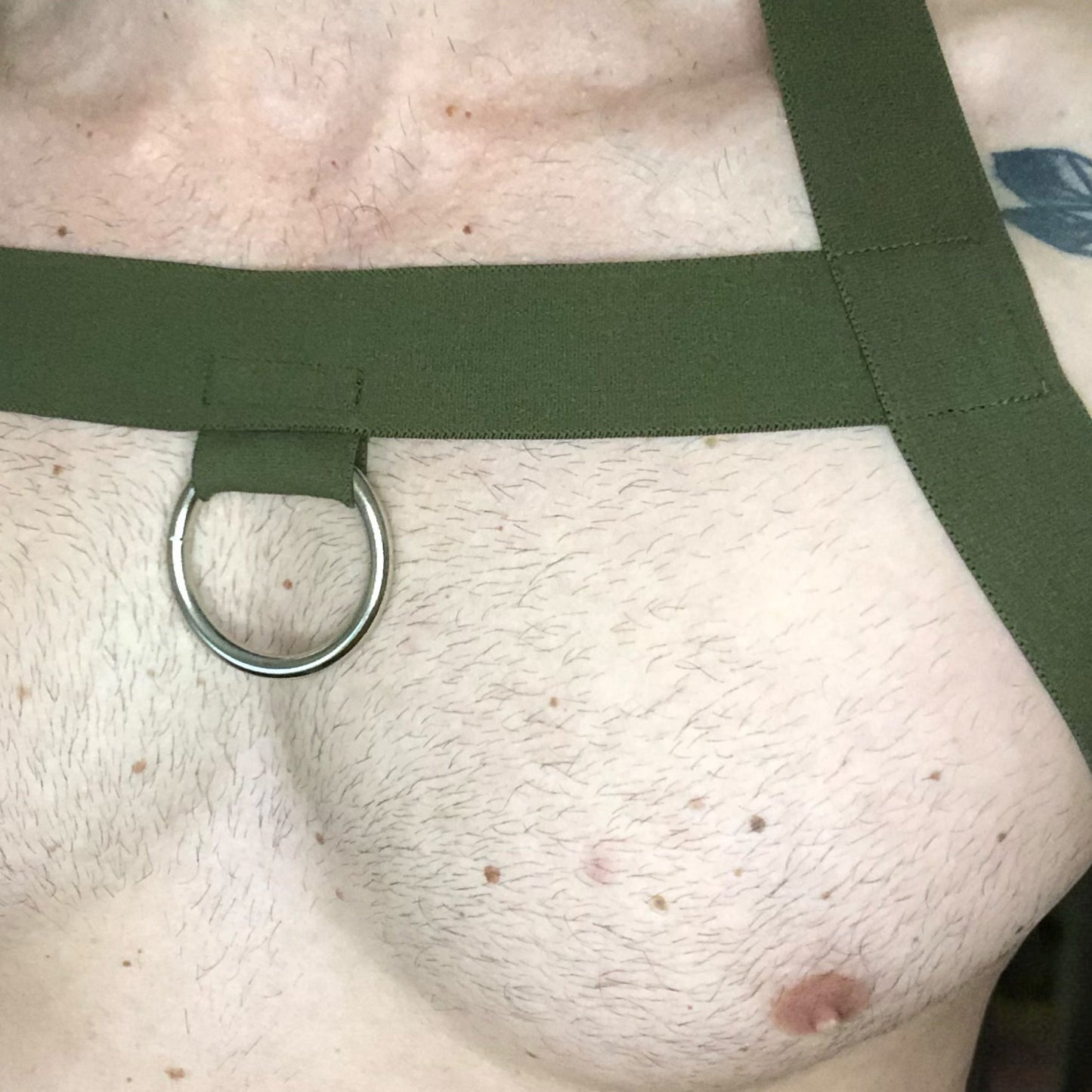 Model wearing a custom-made military green elastic chest harness and black mesh jockstrap by Cheeky Boy Harness. Made-to-measure men's festival and clubwear set designed for pride, circuit parties, and dance events