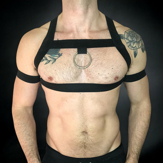 Man wearing a custom-fit black body harness with metal ring and matching bicep bands by CheekyBoyHarness. Festival and clubwear style, handmade to measure