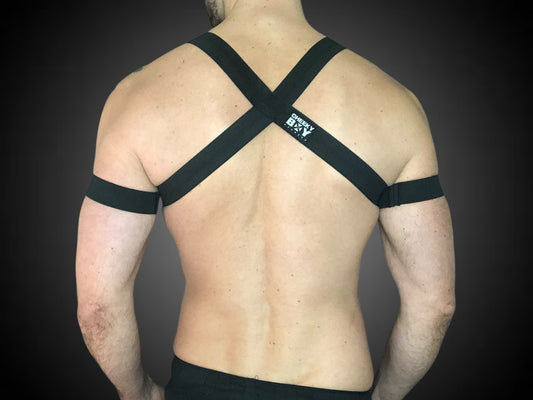 Man wearing a custom-fit black body harness with metal ring and matching bicep bands by CheekyBoyHarness. Festival and clubwear style, handmade to measure