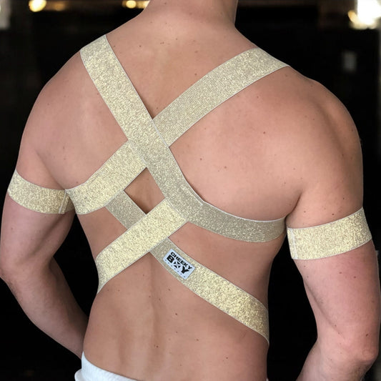 Man wearing a gold elastic full body harness with metal cross over straps on back, metal chest ring, bicep bands, made by Cheeky Boy Harness
