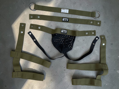 Army green harness shorts and black mesh jockstrap laid flat to show the detachable components
