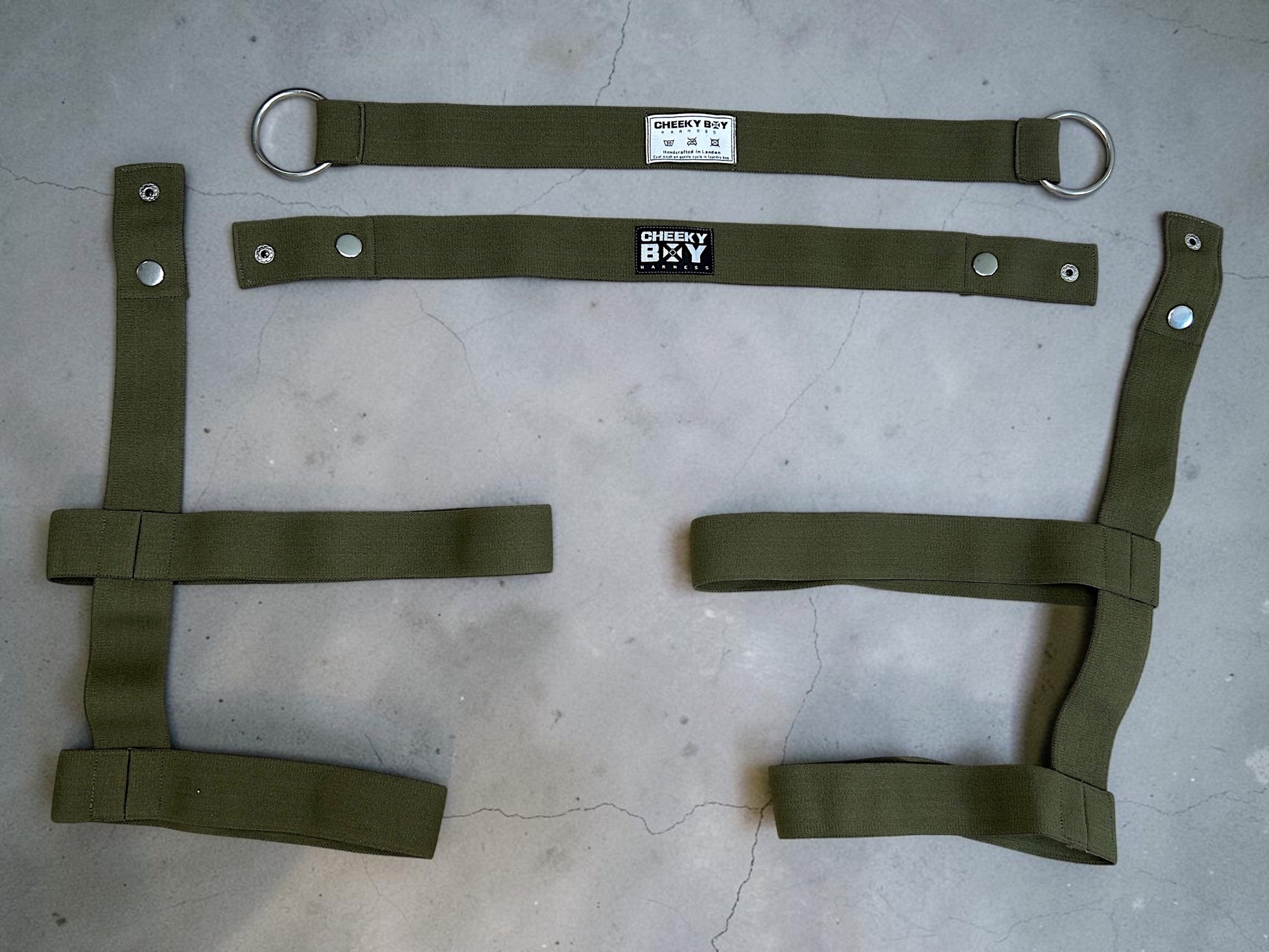 Army green harness shorts laid flat to show the waistband, thigh bands and connecting straps
