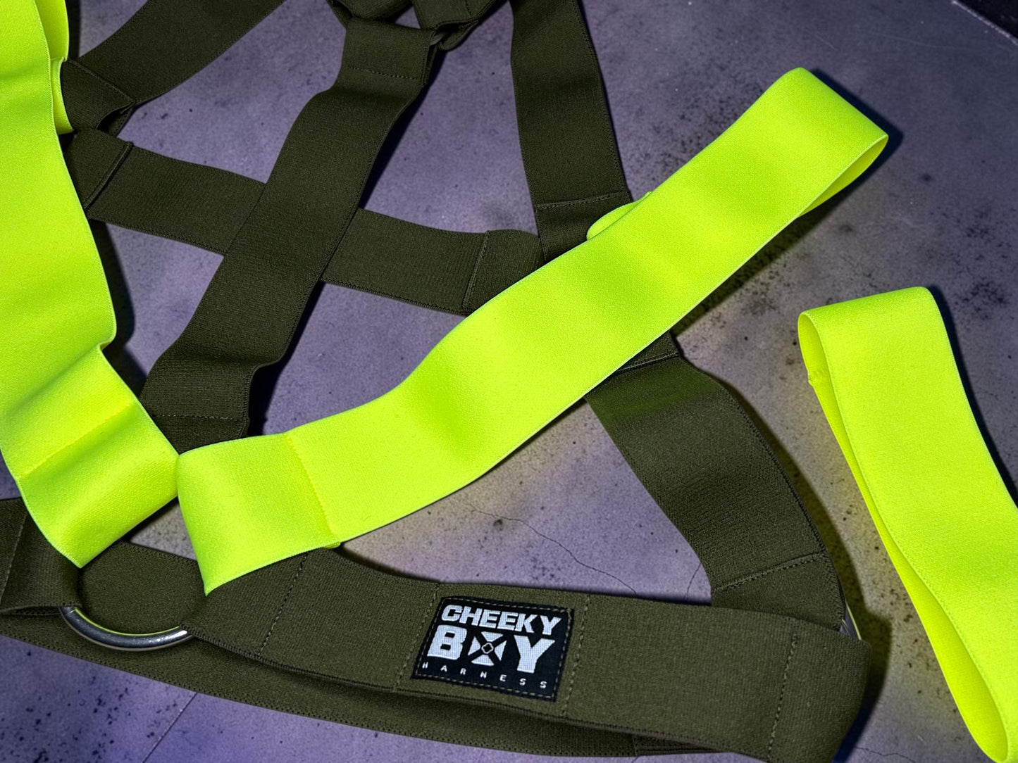 Flat lay of the army green men’s chest harness set with Neon Yellow shoulder sections, matching bands, metal rings and removable lower strap.