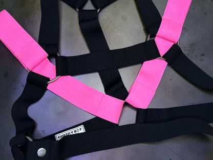 Flat lay of the black elastic men’s chest harness with Neon Pink shoulder sections, silver-tone rings and matching straps and bands.
