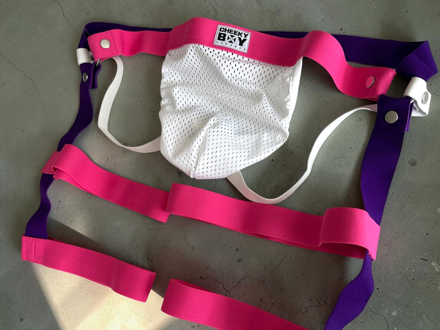 Hot pink elastic harness shorts with white mesh jockstrap pouch laid flat
