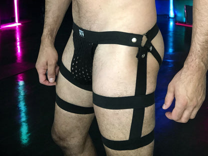Men’s black elastic harness shorts worn over beige underwear in colourful club lighting
