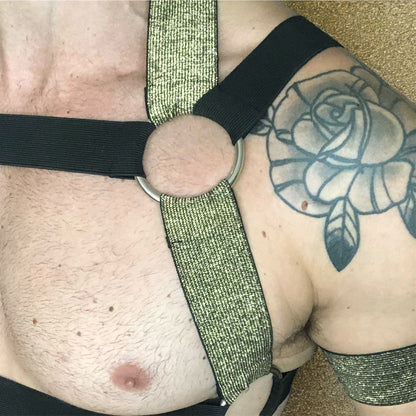 Model wearing a custom-made black & gold elastic body harness with metal rings and matching jockstrap by Cheeky Boy Harness. Includes gold bicep bands and leg straps, designed for clubwear, fetish events, and festivals