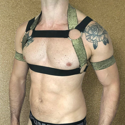 Model wearing a custom-made black & gold elastic body harness with metal rings and matching jockstrap by Cheeky Boy Harness. Includes gold bicep bands and leg straps, designed for clubwear, fetish events, and festivals