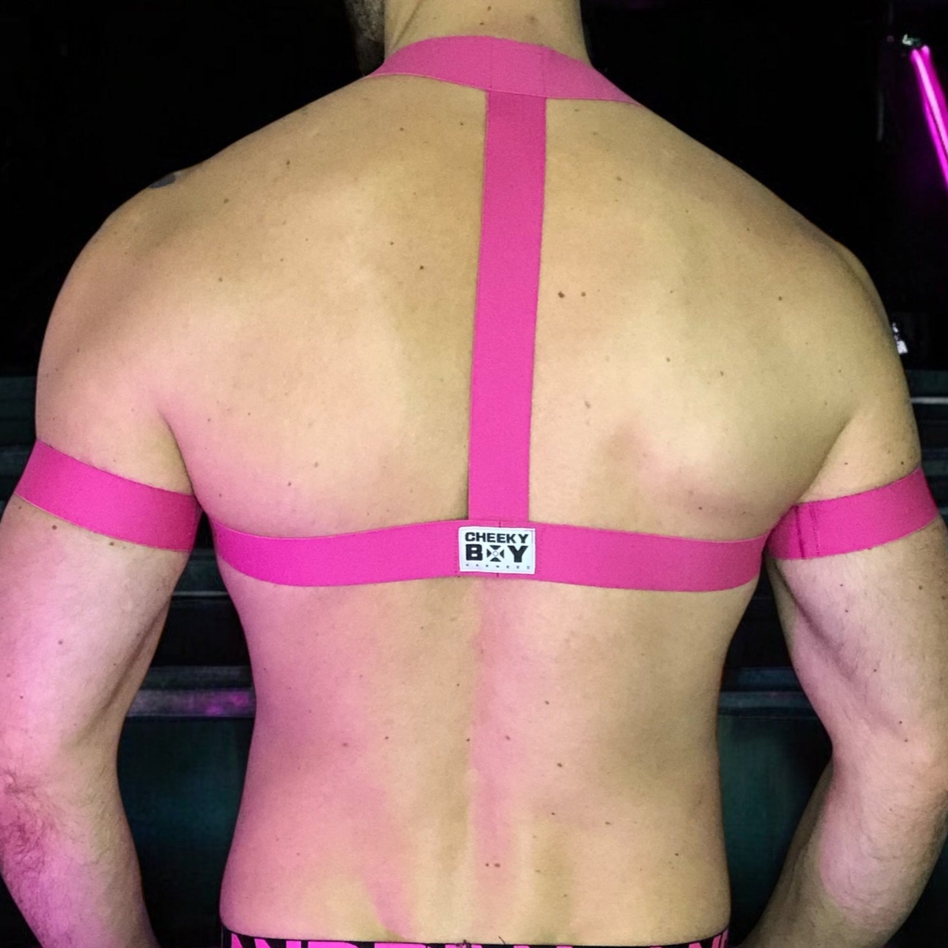 Model wearing a custom-made hot pink elastic chest harness and black mesh jockstrap by Cheeky Boy Harness. Made-to-measure men's festival and clubwear set designed for pride, circuit parties, and dance events