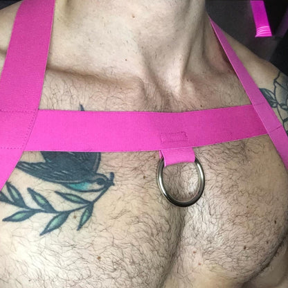 Model wearing a custom hot pink elastic body harness by Cheeky Boy Harness, featuring a silver chest ring, matching bicep bands, and thigh straps, styled with a pink mesh jockstrap.