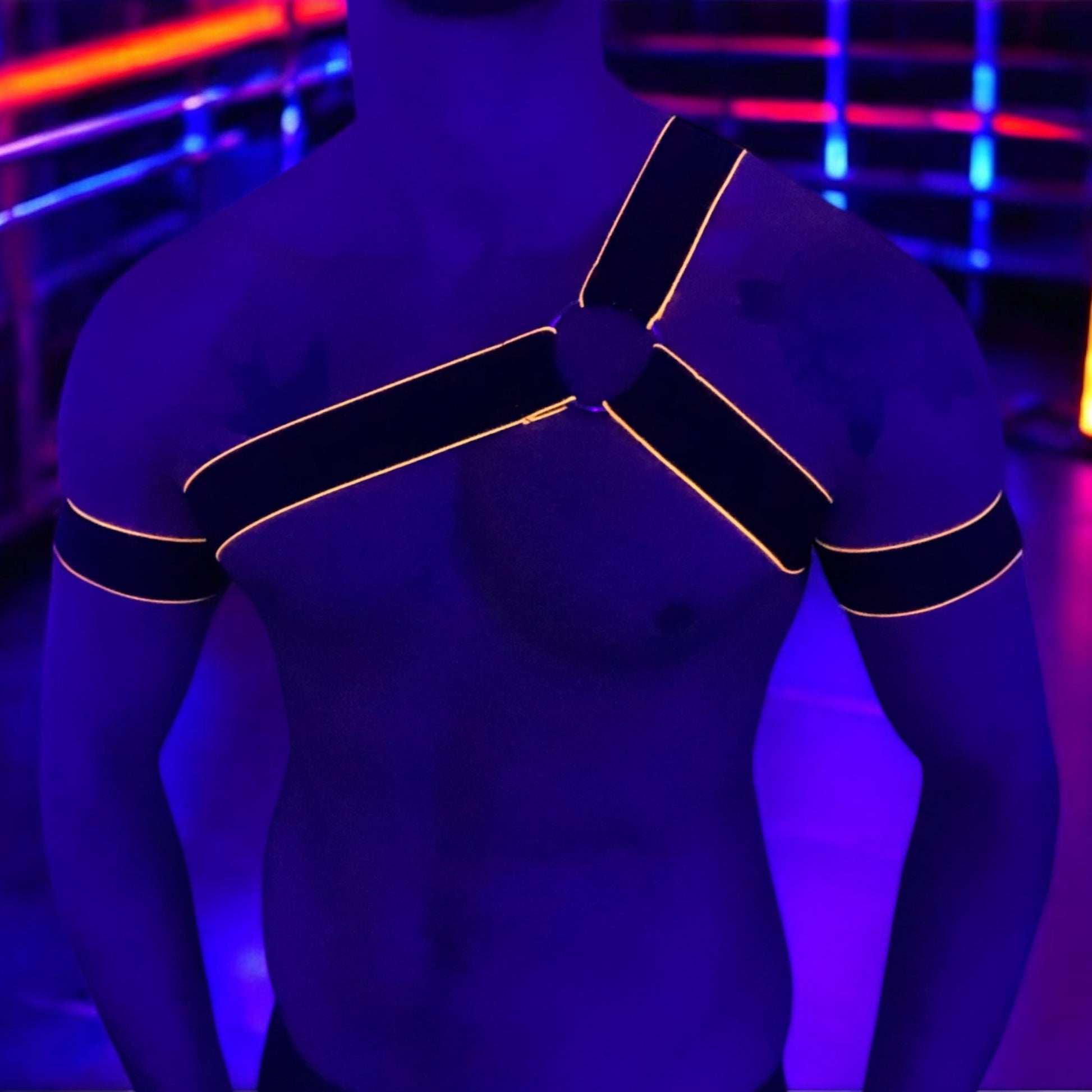 Man wearing a handmade black chest harness with glowing neon orange edges, styled in a Spartan warrior design. Includes matching bicep bands. Photographed in a neon-lit club setting. The harness is made to measure and glows under UV light, ideal for clubbing and festival wear.