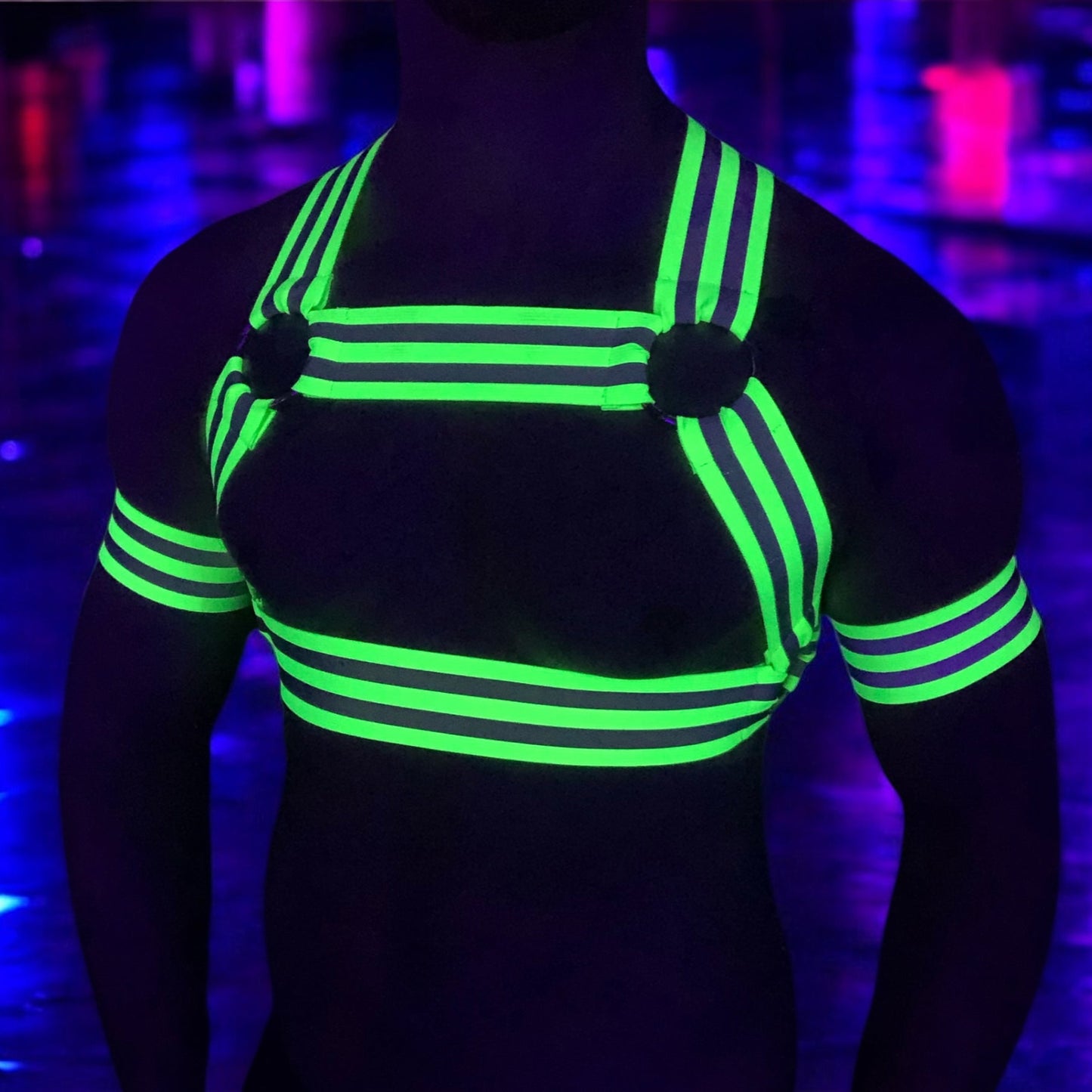 Made-to-measure men’s elastic chest harness in high-visibility neon yellow with reflective detailing, glowing under blacklight. The design features double shoulder and chest straps joined by circular O-rings, with optional matching jockstrap and thigh bands—ideal for clubwear, festivals, or fetish fashion.