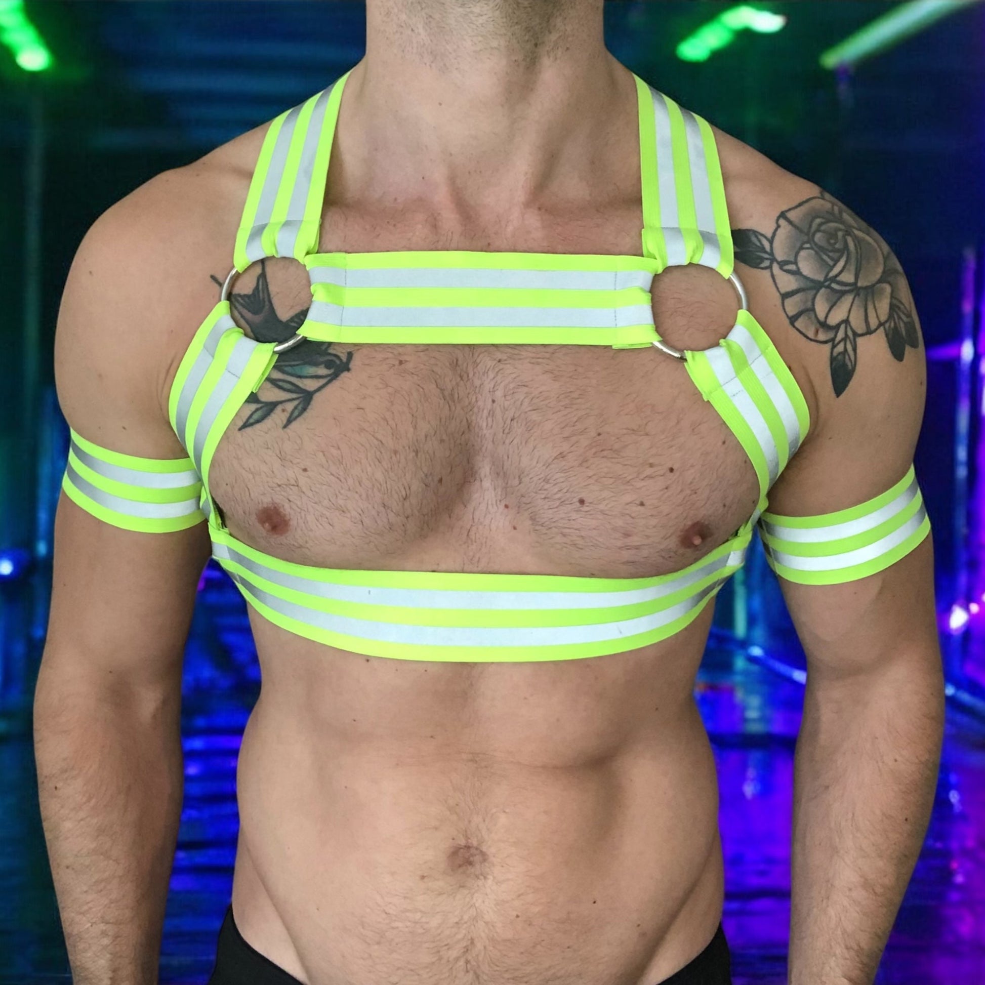 Made-to-measure men’s elastic chest harness in high-visibility neon yellow with reflective detailing, glowing under blacklight. The design features double shoulder and chest straps joined by circular O-rings, with optional matching jockstrap and thigh bands—ideal for clubwear, festivals, or fetish fashion.
