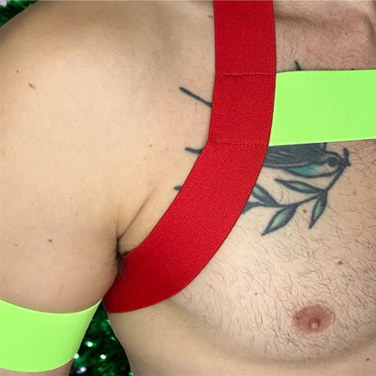 Model wearing a custom-made red and neon green christmas inspired elastic chest harness with black mesh jockstrap by Cheeky Boy Harness. Made-to-measure men's festival and clubwear set designed for pride, circuit parties, and dance events