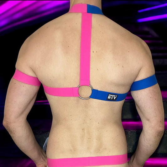 Model wearing a handmade two-tone half pink and half blue full body harness with matching bicep and thigh bands, paired with a white mesh jockstrap, posing in a neon-lit club setting