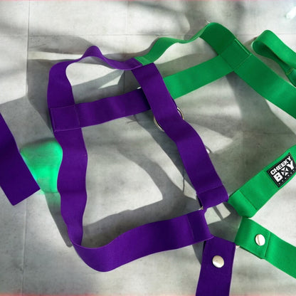Model wearing a handmade two-tone half green and half purple 
 full body harness with matching bicep and thigh bands, paired with a white mesh jockstrap, posing in a neon-lit club setting