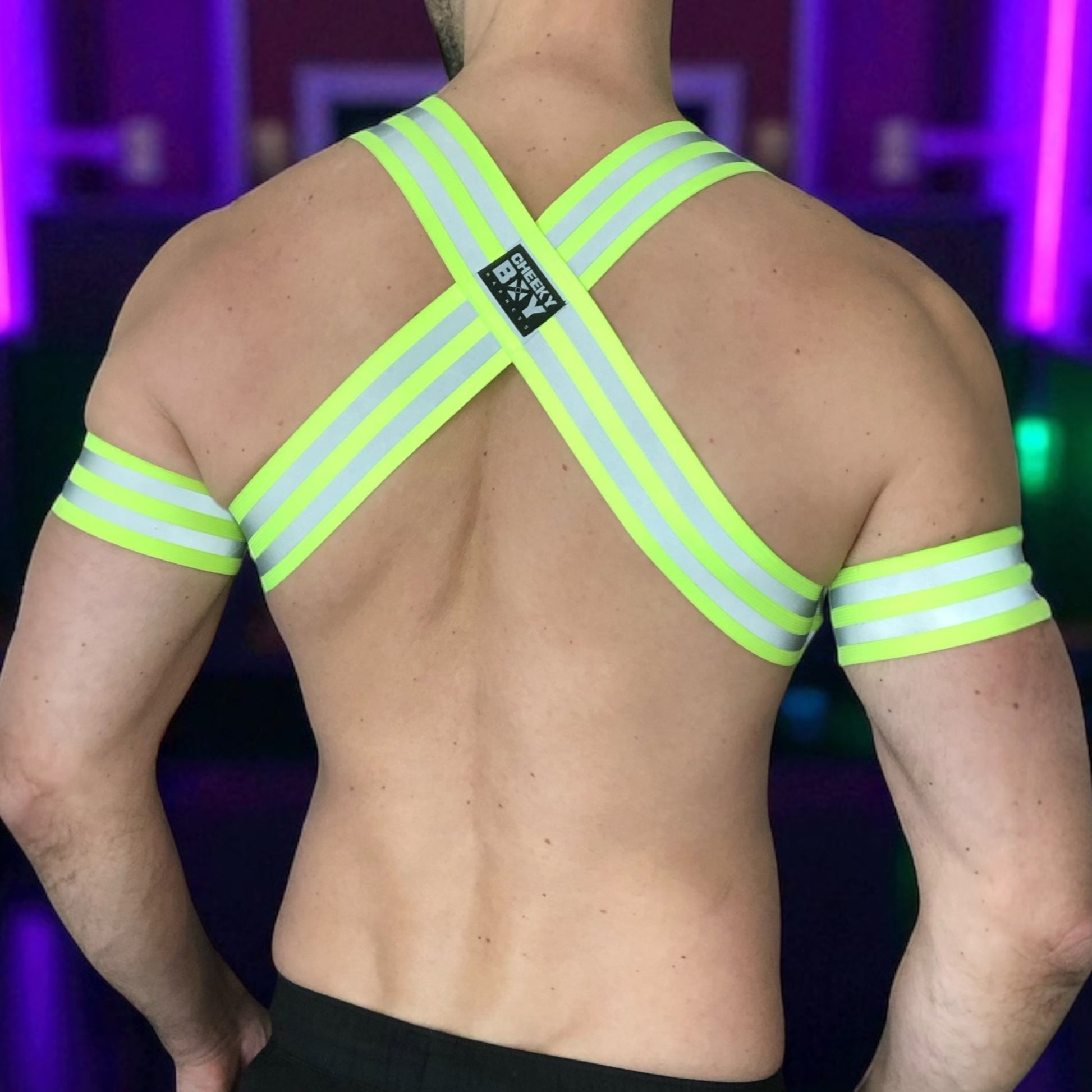 Made-to-measure men’s elastic chest harness in high-visibility neon yellow with reflective detailing, glowing under blacklight. The design features double shoulder and chest straps joined by circular O-rings, with optional matching jockstrap and thigh bands—ideal for clubwear, festivals, or fetish fashion.