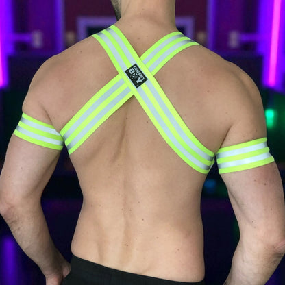 Made-to-measure men’s elastic chest harness in high-visibility neon yellow with reflective detailing, glowing under blacklight. The design features double shoulder and chest straps joined by circular O-rings, with optional matching jockstrap and thigh bands—ideal for clubwear, festivals, or fetish fashion.