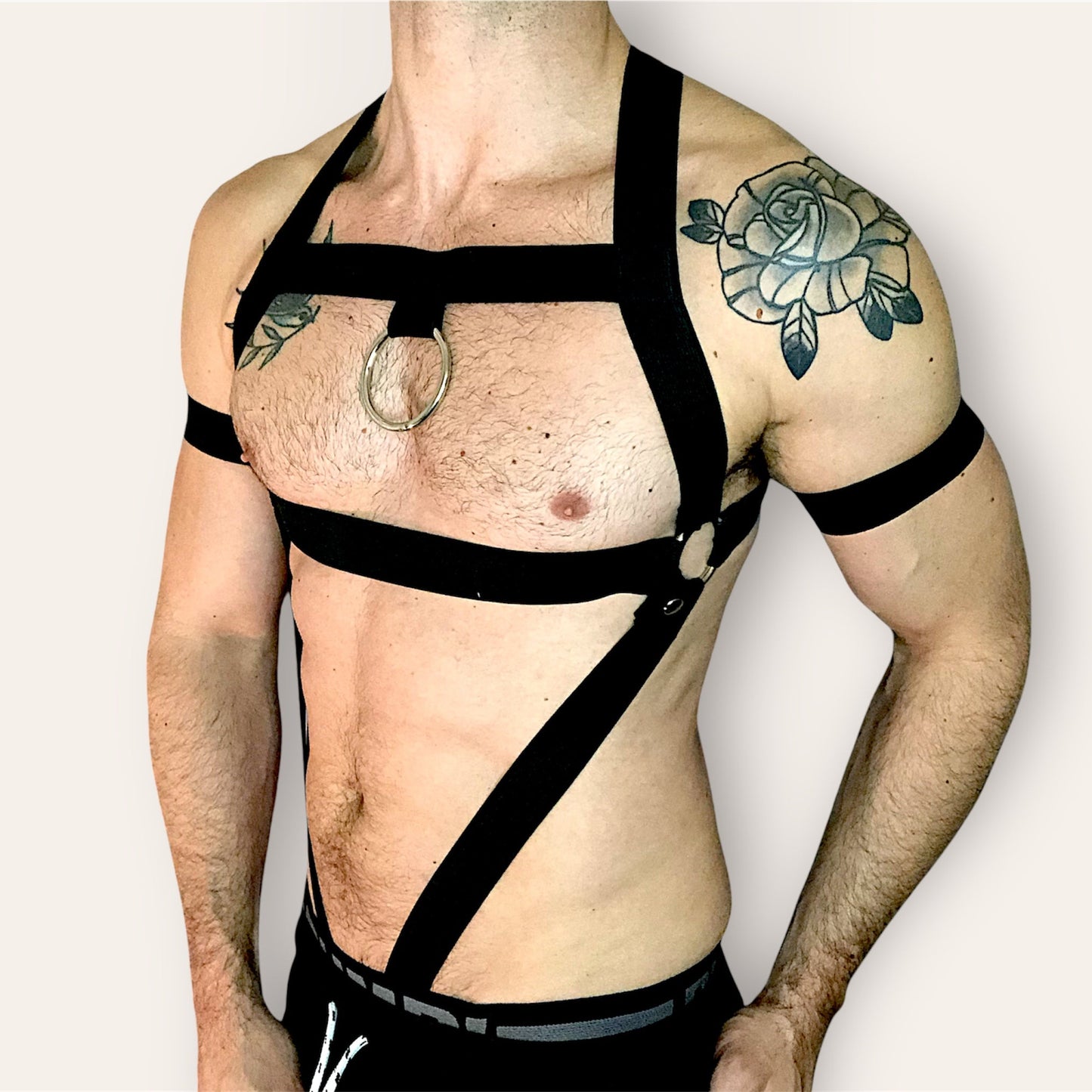 Man wearing a custom-fit black body harness with metal ring and matching bicep bands by CheekyBoyHarness. Gay clubwear, rave outfit, made to measure