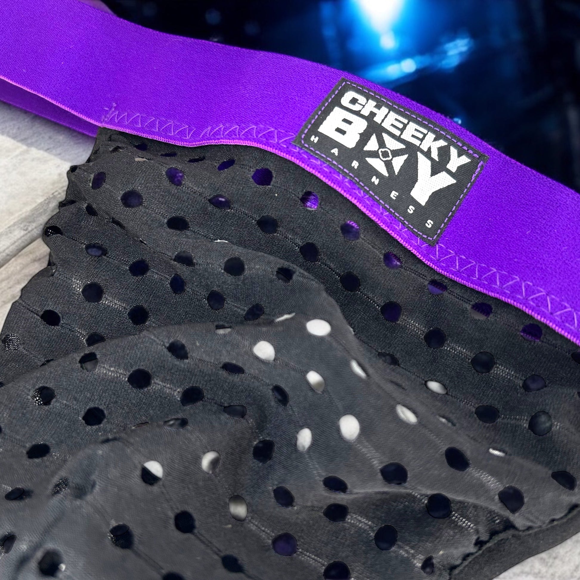 Man wearing a custom-fit purplr elastic chest and body harness with matching bicep bands, featuring metal ring details and diagonal strap design. Styled with black mesh jockstrap underwear. Handmade by Cheeky Boy Harness