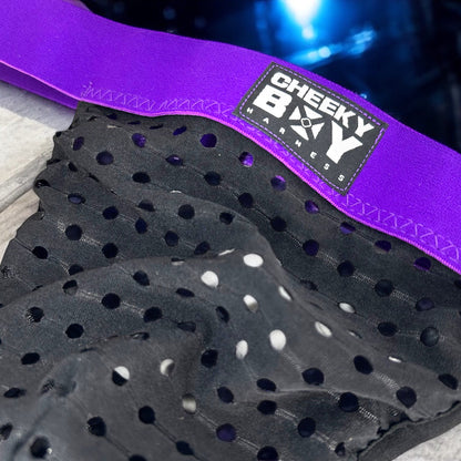 Man wearing a custom-fit purplr elastic chest and body harness with matching bicep bands, featuring metal ring details and diagonal strap design. Styled with black mesh jockstrap underwear. Handmade by Cheeky Boy Harness