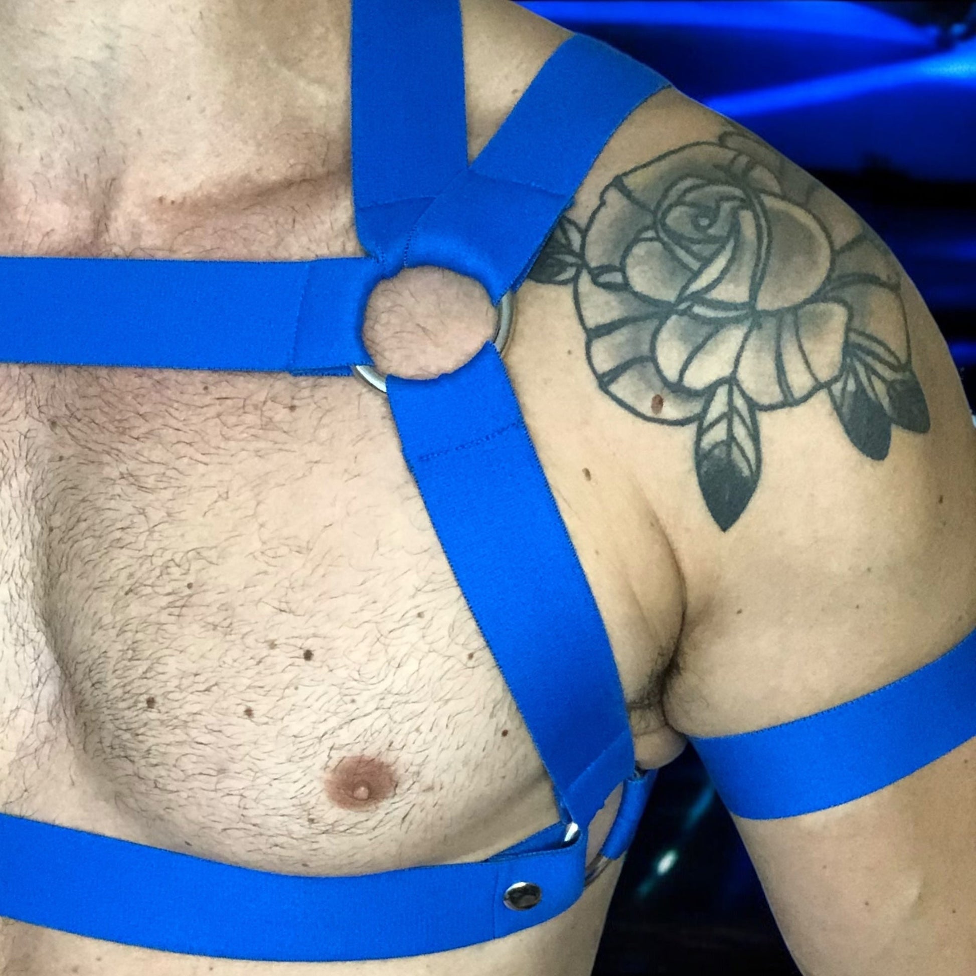 Man Wearing a Made-To-Measure Royal Blue Elastic Chest Harness with Metal Rings and Matching Bicep Bands, Club Background, Custom Fit Design by Cheeky Boy Harness