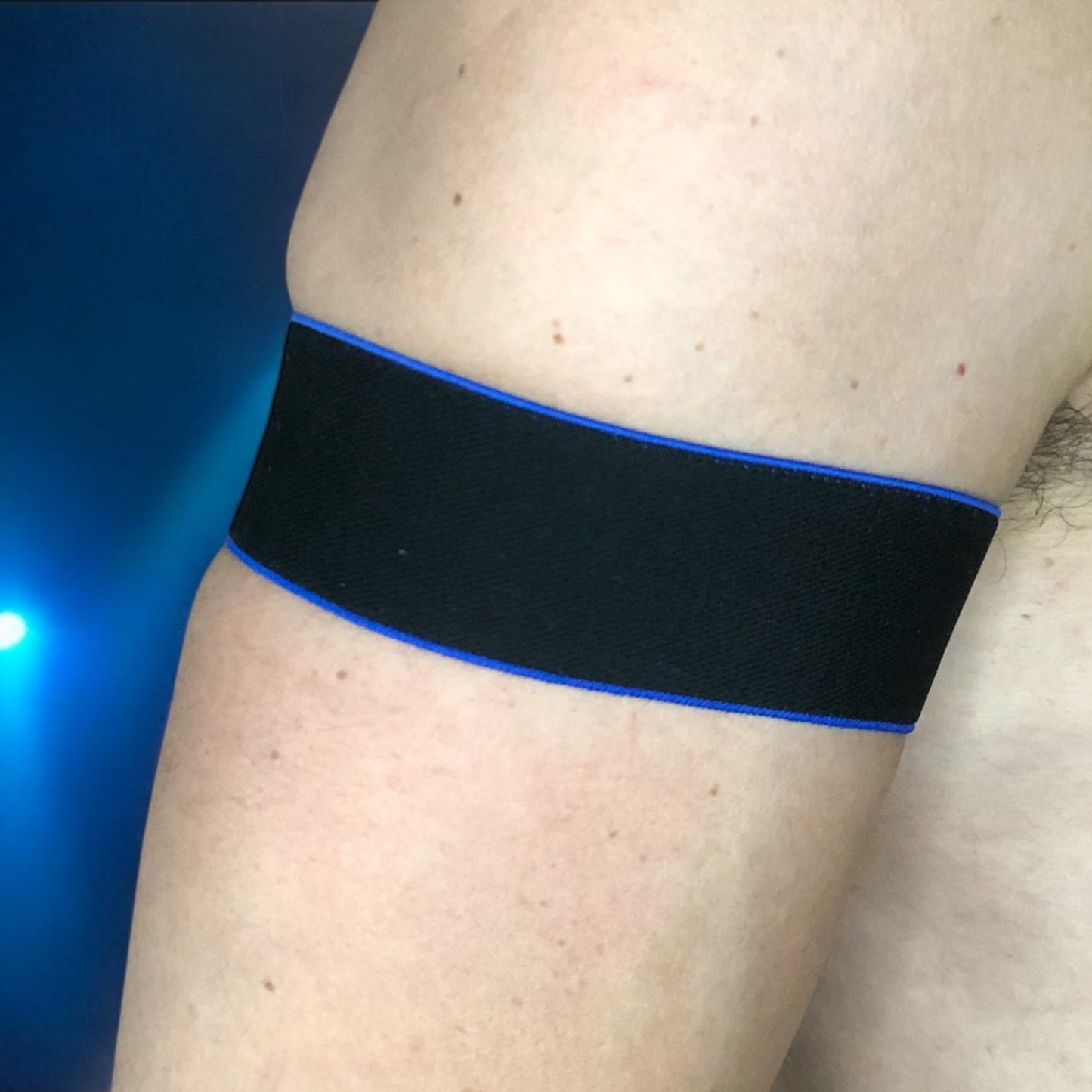 Man wearing a handmade black chest harness with glowing neon orange edges, styled in a Spartan warrior design. Includes matching bicep bands. Photographed in a neon-lit club setting. The harness is made to measure and glows under UV light, ideal for clubbing and festival wear.