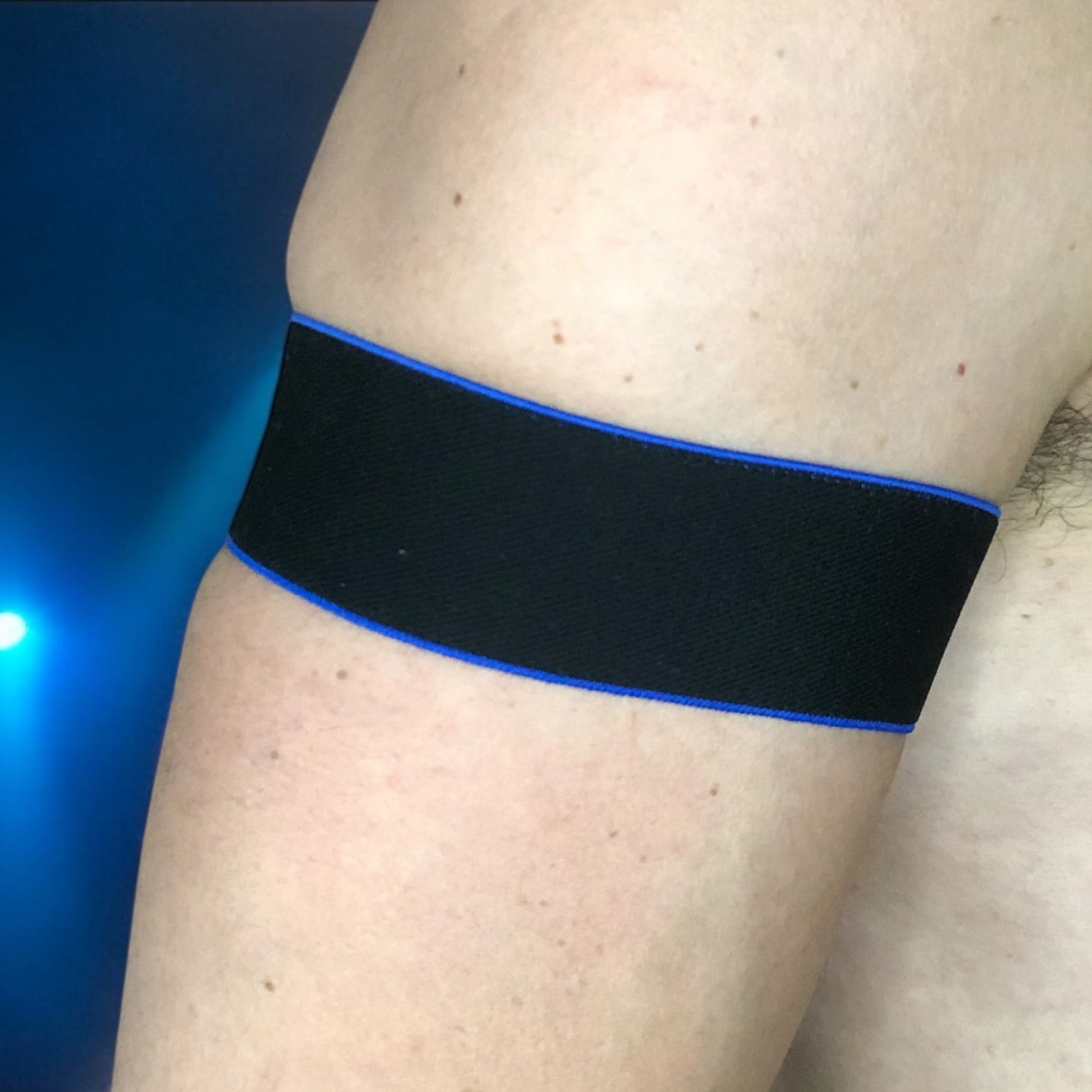 Man wearing a handmade black chest harness with glowing neon orange edges, styled in a Spartan warrior design. Includes matching bicep bands. Photographed in a neon-lit club setting. The harness is made to measure and glows under UV light, ideal for clubbing and festival wear.