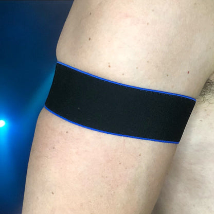 Man wearing a handmade black chest harness with glowing neon orange edges, styled in a Spartan warrior design. Includes matching bicep bands. Photographed in a neon-lit club setting. The harness is made to measure and glows under UV light, ideal for clubbing and festival wear.