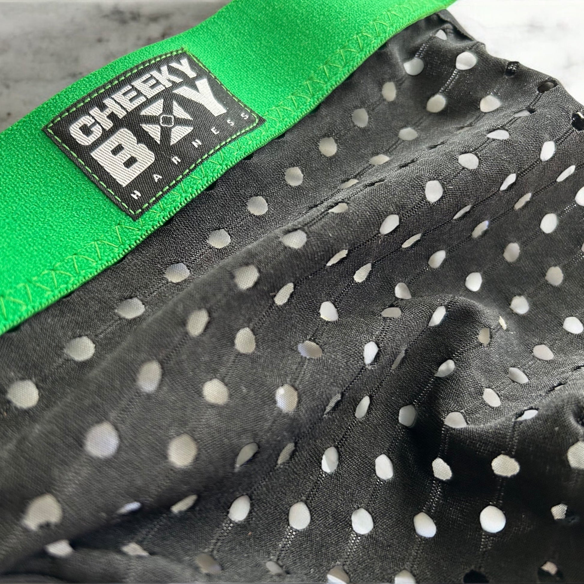 Men’s black mesh jockstrap with green elastic waistband, featuring a Cheeky Boy Harness black and white logo at the centre front, and black rear straps.