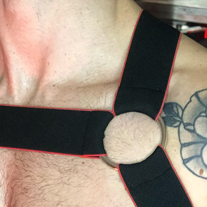 Toned model Wearing Made-to-Measure Black and Red Elastic Chest Harness with Metal Rings by Cheeky Boy Harness, Styled for Fetish Clubwear in Red-Lit Venue