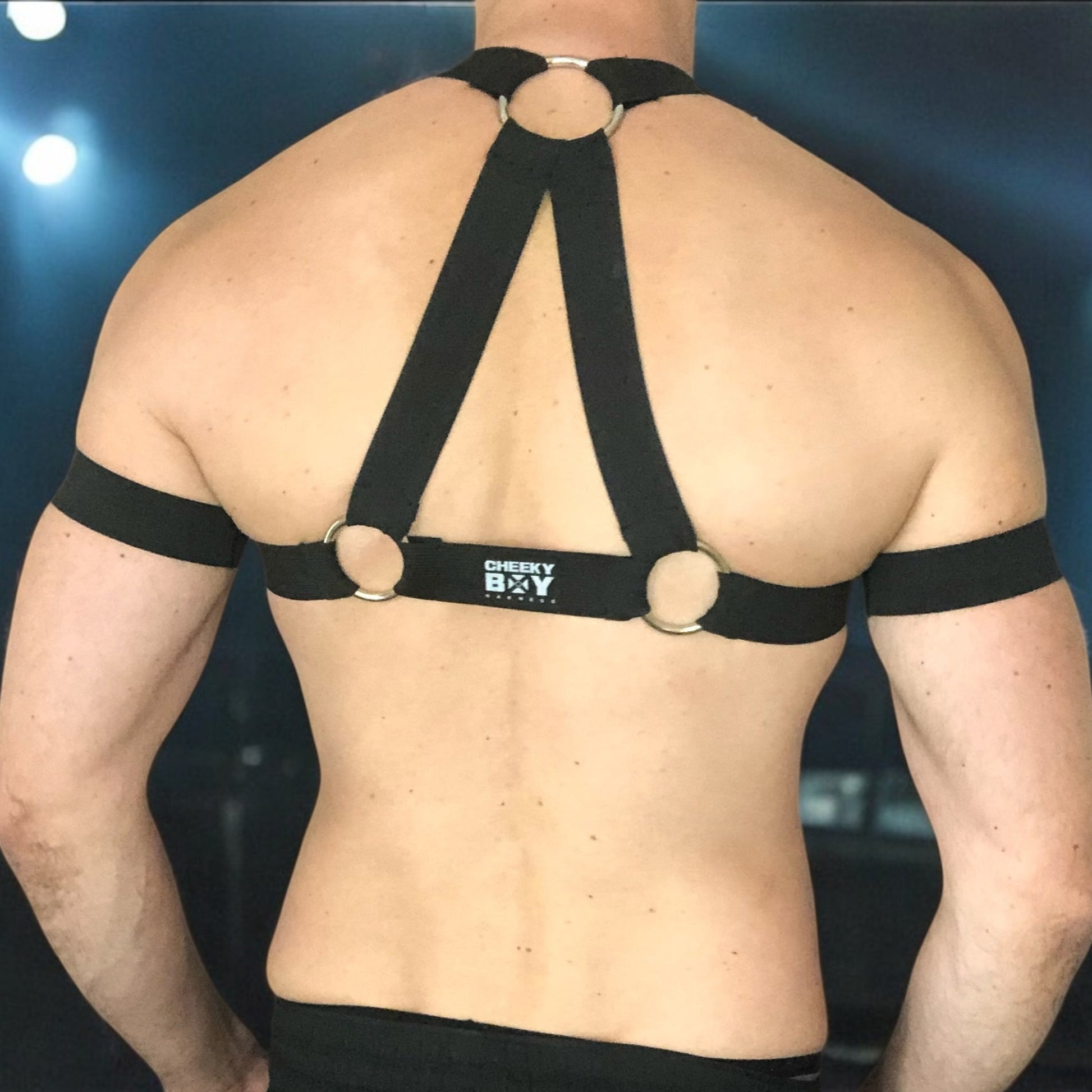 Model wearing a black elastic full body harness with metal rings and matching jockstrap, handmade by Cheeky Boy Harness – custom fit for clubwear, pride, and fetish events
