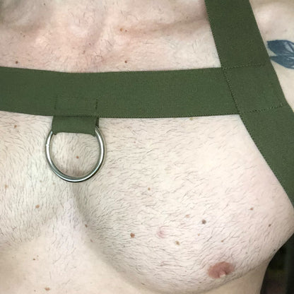 Model wearing a custom-made military green elastic chest harness and black mesh jockstrap by Cheeky Boy Harness. Made-to-measure men's festival and clubwear set designed for pride, circuit parties, and dance events