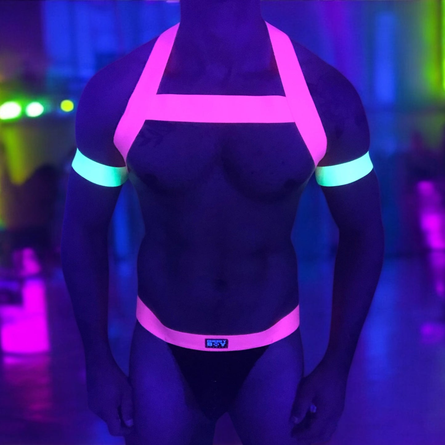 Model wearing a neon yellow chest harness with matching neon pink bicep bands and waistband jockstrap by Cheeky Boy Harness. Customisable colour options available. Perfect for festivals, clubwear, and pride events.