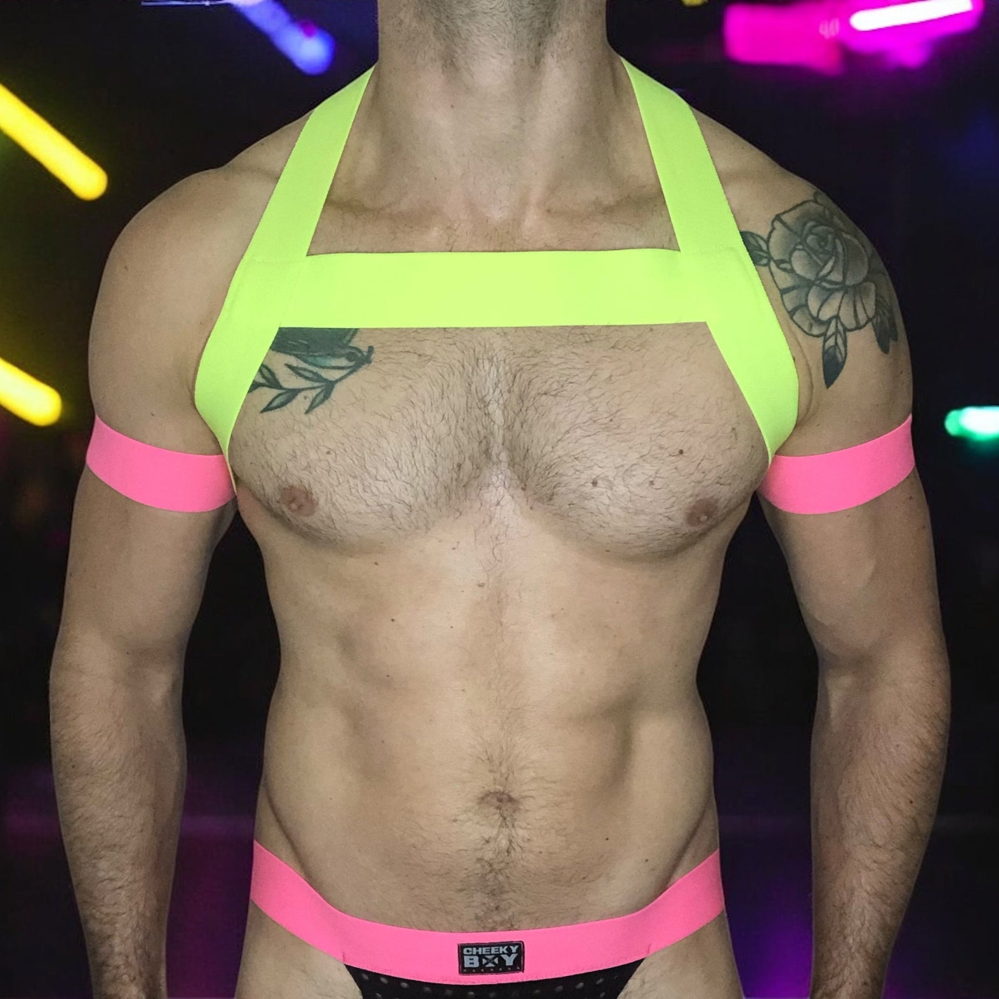 Model wearing a neon yellow chest harness with matching neon pink bicep bands and waistband jockstrap by Cheeky Boy Harness. Customisable colour options available. Perfect for festivals, clubwear, and pride events.