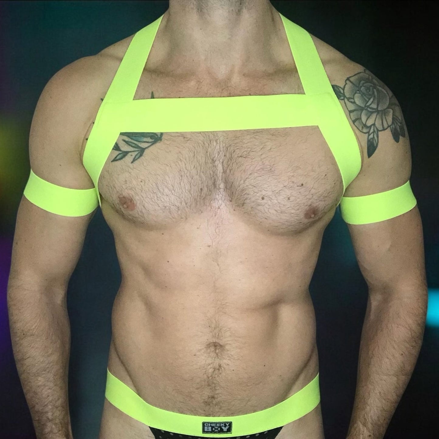 Model wearing a neon yellow chest harness with matching neon pink bicep bands and waistband jockstrap by Cheeky Boy Harness. Customisable colour options available. Perfect for festivals, clubwear, and pride events.