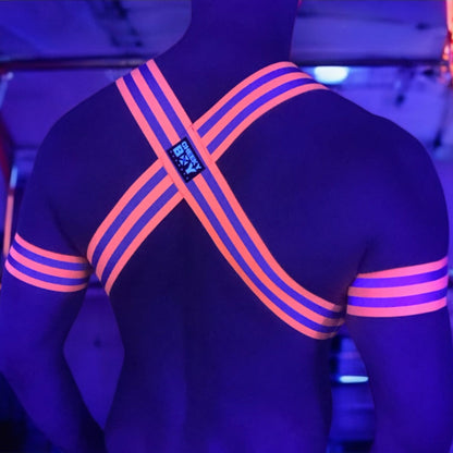 Made-to-measure men’s elastic chest harness in high-visibility neon orange with reflective detailing, glowing under blacklight. The design features double shoulder and chest straps joined by circular O-rings, with optional matching jockstrap and thigh bands—ideal for clubwear, festivals, or fetish fashion.