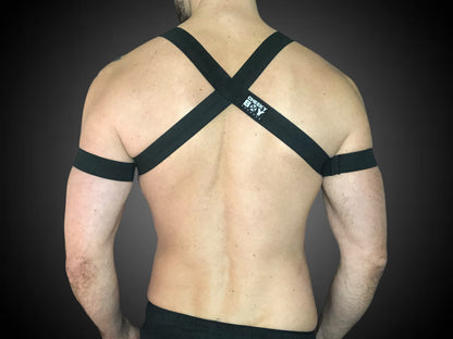 Man wearing a custom-fit black body harness with metal ring and matching bicep bands by CheekyBoyHarness. Festival and clubwear style, handmade to measure