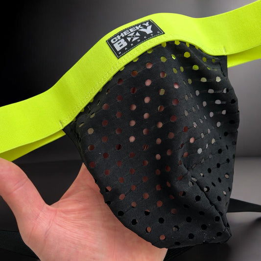 Model wearing a custom-made neon yellow and pink elastic chest harness with matching jockstrap and bicep bands by Cheeky Boy Harness, photographed in a glowing club setting. Made-to-measure for a perfect fit, ideal for festivals, clubwear, and pride events