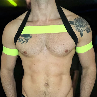 A man wearing a handmade, made-to-measure black and neon yellow elastic chest harness with matching jockstrap and bicep bands by Cheeky Boy Harness.
