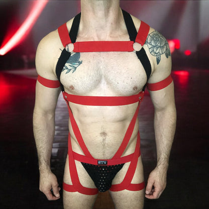 Model wearing a custom-made red and black elastic chest harness with metal rings and matching jockstrap by Cheeky Boy Harness. Includes red bicep bands. Designed for clubwear, raves, fetish events, and festivals