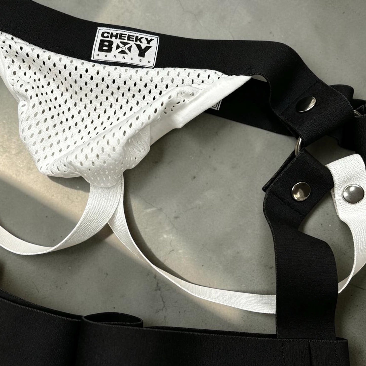 Close-up comparison of the optional black and white Mesh Jockstrap pouches with Cheeky Boy Harness branding and detachable clips.