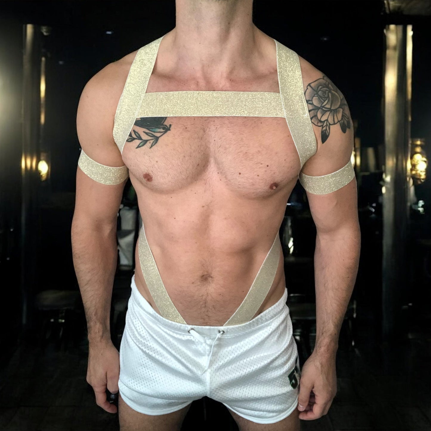Man wearing a gold elastic full body harness with metal cross over straps on back, metal chest ring, bicep bands, made by Cheeky Boy Harness