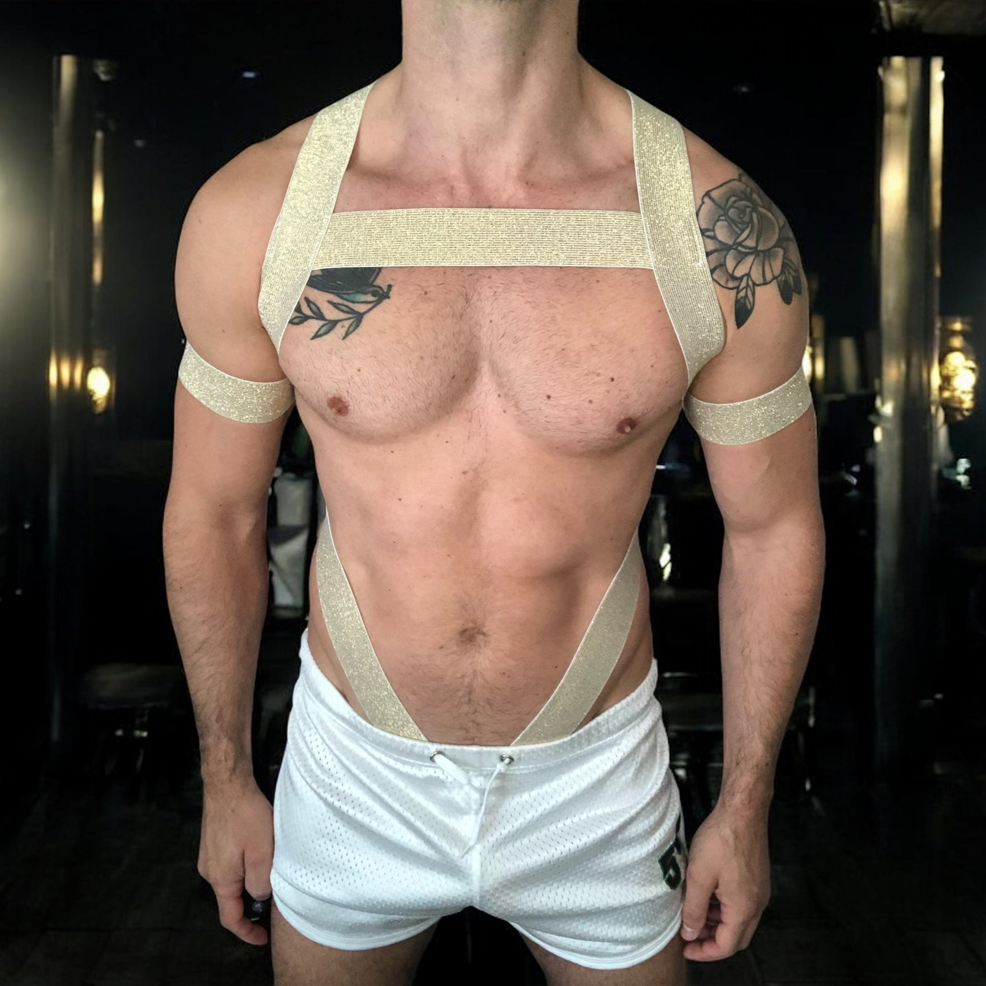 Man wearing a gold elastic full body harness with metal cross over straps on back, metal chest ring, bicep bands, made by Cheeky Boy Harness