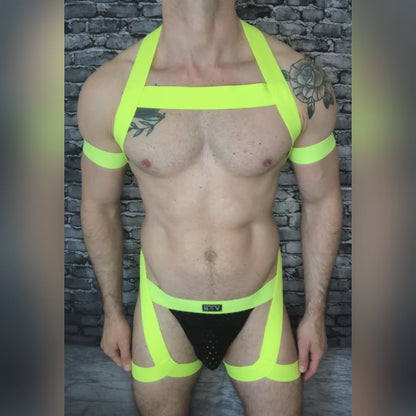Model wearing a custom-made neon yellow and pink elastic chest harness with matching jockstrap and bicep bands by Cheeky Boy Harness, photographed in a glowing club setting. Made-to-measure for a perfect fit, ideal for festivals, clubwear, and pride events